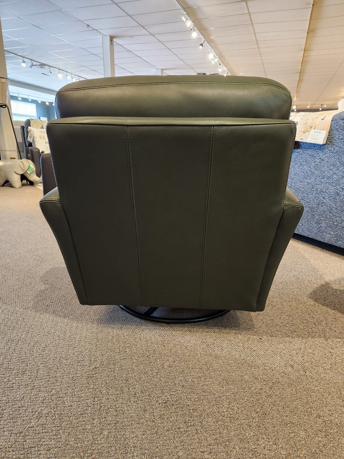 The Leather Craft 745 Leather Swivel Rocker Chair is shown from the back in a carpeted furniture showroom.