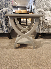 The Durham 900-532 Transitional Chairside End Table with curved X-legs sits on carpet between patterned armchairs.