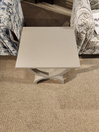 The Durham 900-532 Transitional Chairside End Table with decorative base stands between two patterned chairs on carpet.