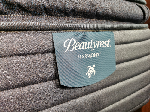 Close-up of a Beauty-rest Deepwater Pillow Top Firm Mattress label on a gray fabric covering.