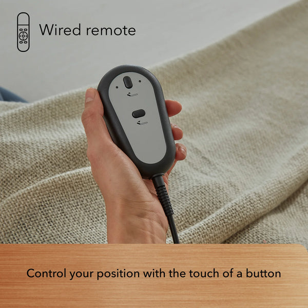 A hand holds a wire remote with arrows, operating the Beauty-Rest Bronze Adjustable Base above a beige textured surface.