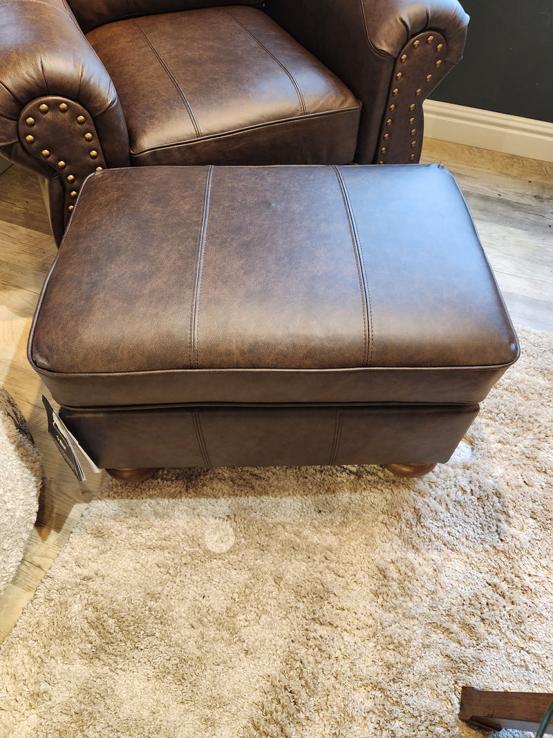 The Best F24ELU Noble Leather Ottoman sits on a beige rug before a matching studded armchair.