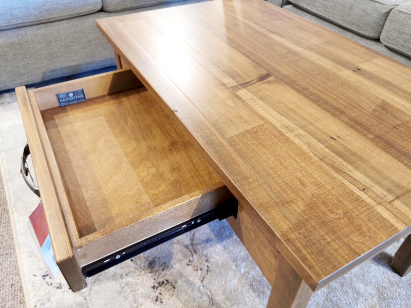 The Handstone GG2135 Glengarry Condo Coffee Table with Drawer sits open on a light rug before a gray sofa.