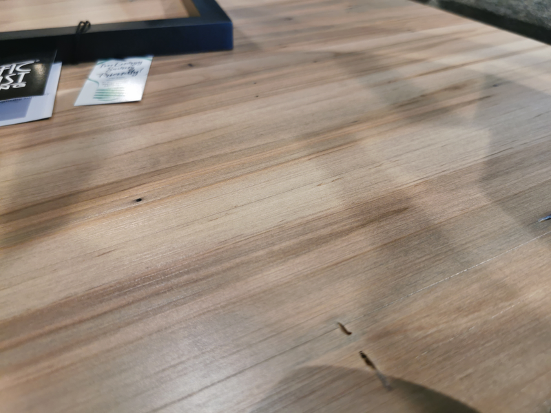 Close-up of Handstone's N-gg24 Glengarry End Table's wooden surface with small holes, cards, and a blue frame visible.