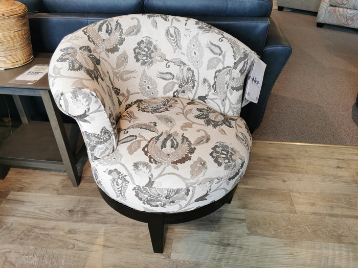 The Attica Swivel Chair by Best, featuring a cottage-style design with a floral pattern, sits on a wooden floor and brings a cozy touch to the space beside the blue sofa and side table.