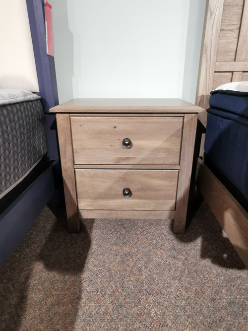 The 123 Custom Express Nightstand by Vaughan Bassett, in driftwood grey, with two drawers sits between the beds on carpet.