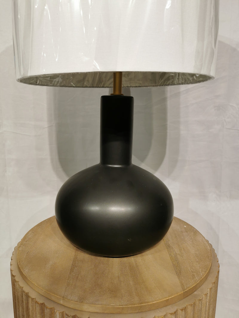 The Crestview Collection Griffith Table Lamp has a matte ceramic base, white shade, and sits on a round wooden surface.