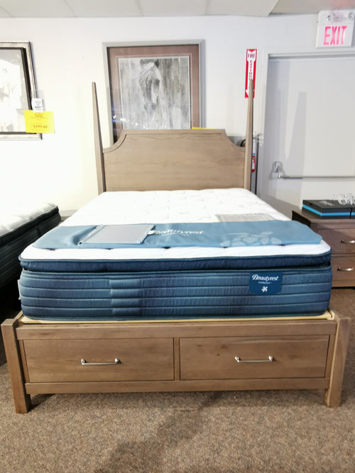 The Vaughan Bassett 831 Pencil Post Tide & Timber Queen Bed with quilted mattress is displayed, artwork and exit sign in background.