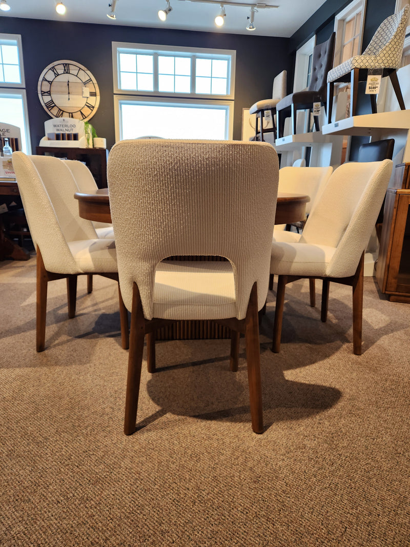 Six Handstone Lotus Dining Package chairs surround a round pedestal table in a showroom with carpeted flooring.