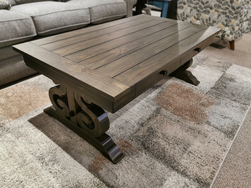 The 2491 Bellamy Cocktail Table by Magnussen with scroll base stands on a patterned rug in the living room.