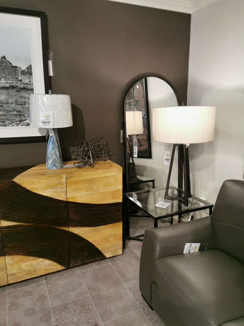 A modern living room with a wood cabinet, two lamps, and the Mercana Agatha Full Length Arc Mirror above a gray armchair.