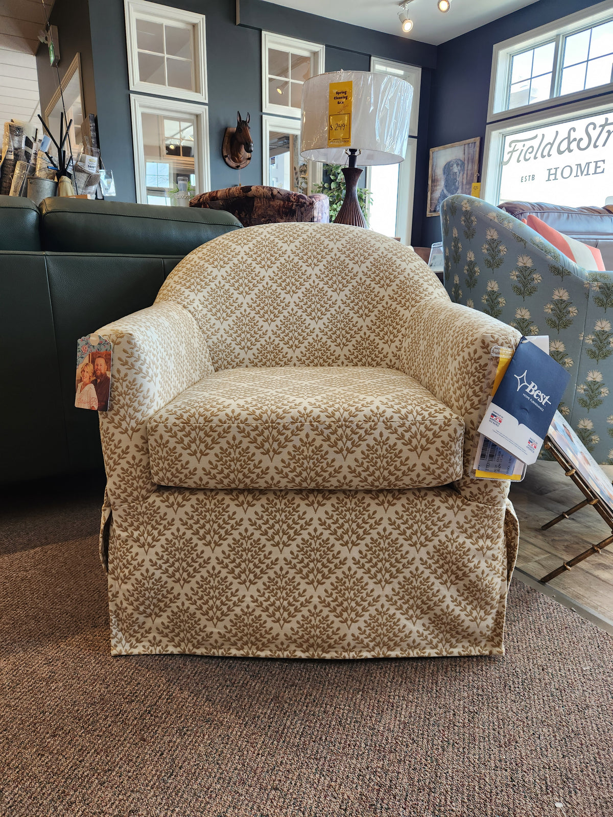 Meg Swivel Chair by Best, patterned beige with tags and a slipcover-style skirt, on display in a furniture store.