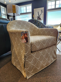 Meg Swivel Chair by Best features a beige patterned barrel back and skirt, shown in-store with two people on armrest.