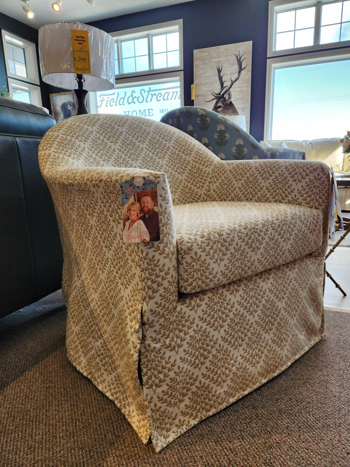 Meg Swivel Chair by Best features a beige patterned barrel back and skirt, shown in-store with two people on armrest.