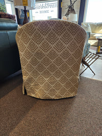 The Meg Swivel Chair by Best, with a repeating leaf pattern, sits on a brown carpet in a sunlit room.