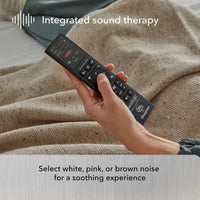 A hand holds a remote on a brown blanket, highlighting Beauty-Rest’s Platinum Adjustable Base with sound therapy features.