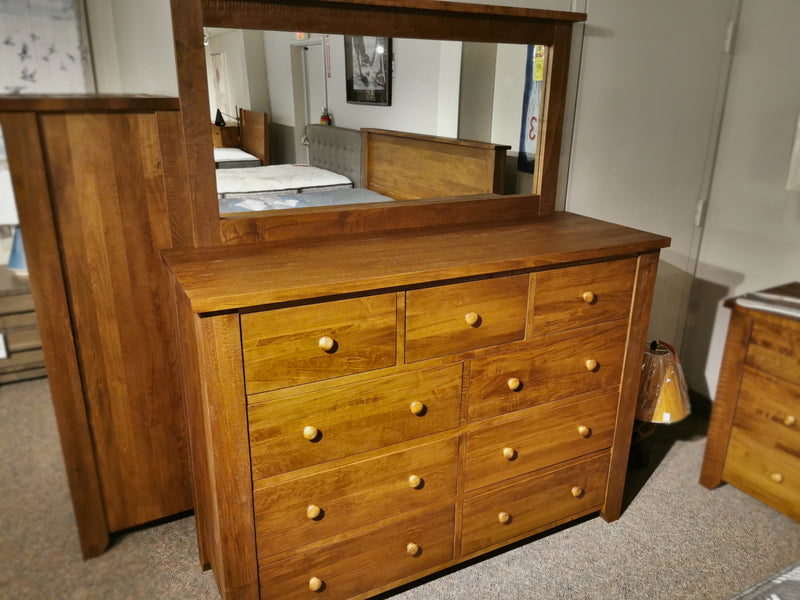 The Vokes 250 Rough Sawn 9-Drawer Dresser features round knobs and a large mirror, shown in a showroom display.
