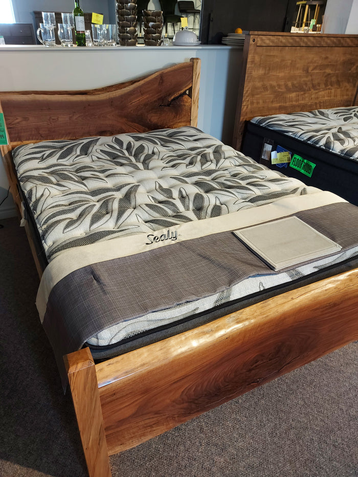 A wooden bed frame with a Sealy Sunset Vista Mattress featuring a euro pillow top and patterned leaf-design cover.