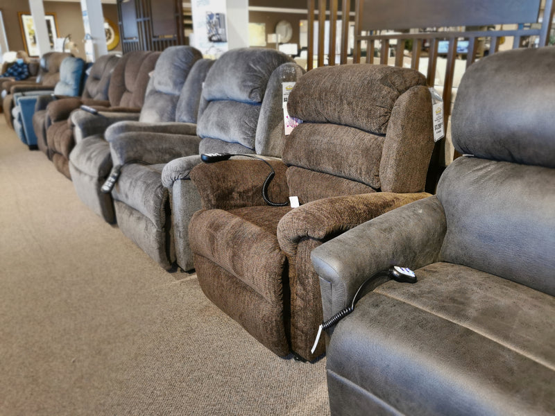 Row of Ultra Comfort Polaris Power Lift Recliners in brown and gray, each with a remote, at a furniture store.