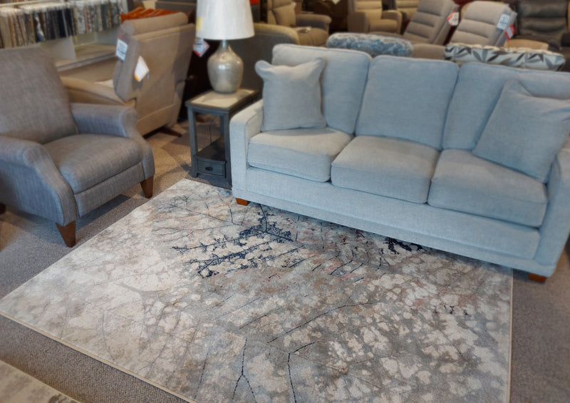 Gray sofa, armchair, lamp on black side table, and Kalora Abbey 3301/160 rug in a furniture showroom.