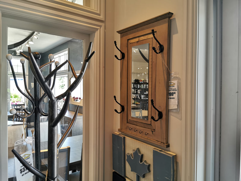 In the store, Woodcraft's 712 Doorganizer is elegantly displayed. This wooden wall-mounted mirror with coat hooks features a vintage grey stain and is priced at $199.99. Alongside it, a partially visible coat rack offers smart 2-D space storage solutions while complementing the functional and stylish design of this piece.
