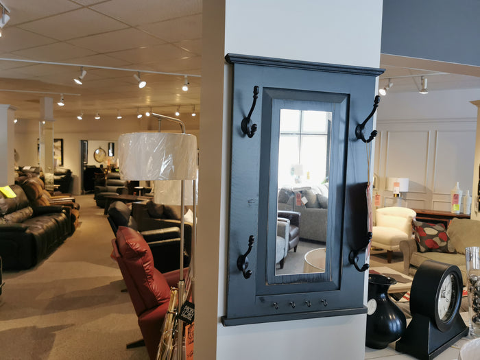 A furniture store showroom features a selection of sofas and chairs, with a wall adorned with mirrors and hooks. Prominently displayed in the foreground is the 712 Doorganizer by Woodcraft, expertly crafted with a vintage grey stain for stylish 2-D space storage.